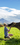 A young girl is sitting on the grass and petting a cow; it looks like the cow is smelling her face.