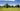 A small herd of Jersey cows grazing on lush green pastures amongst green trees with blue skies and a few small white clouds.