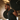 An African American man is doing barbell squats. He has short hair and a well-manicured short beard and mustache. He is wearing a dark grey T-shirt. It looks like he is exercising in a warehouse-style gym from the metal roof.